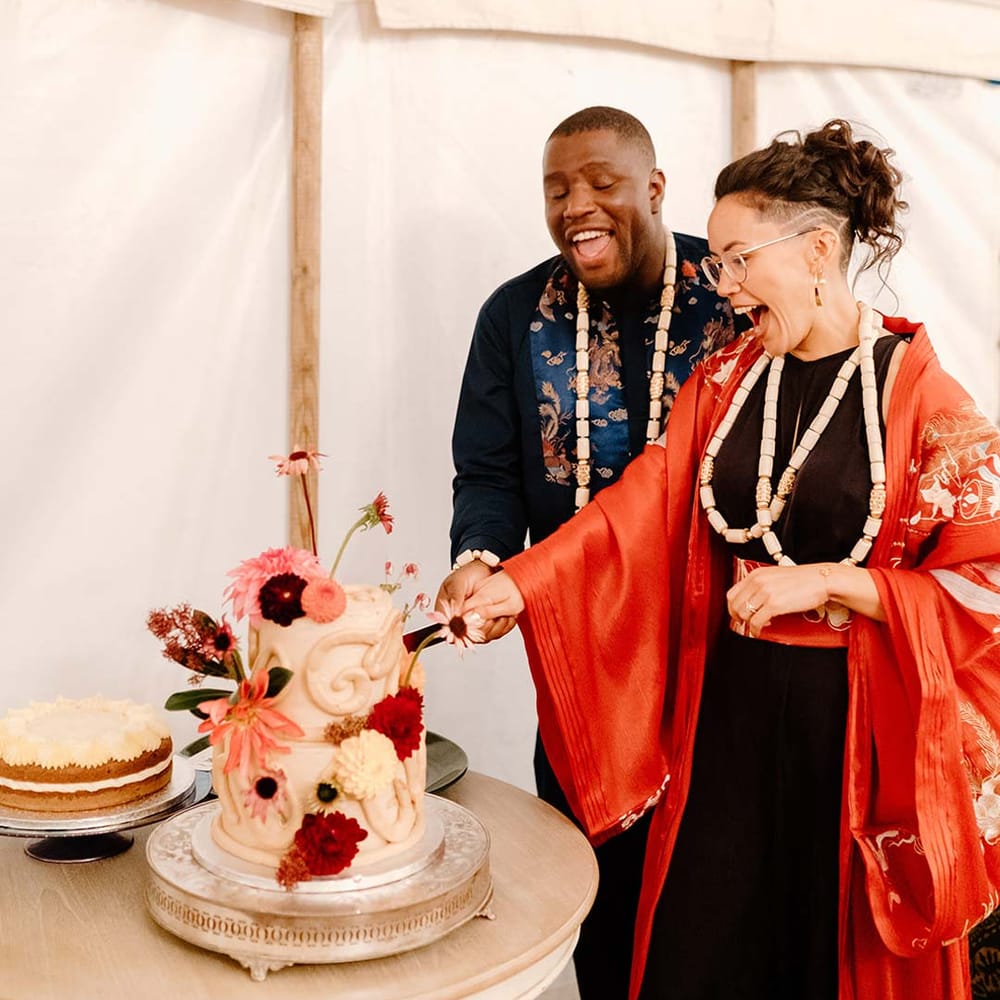 Bride in traditional Chinese wedding kimono standing with groom in navy wedding suit cutting the cake at Broadfield Court