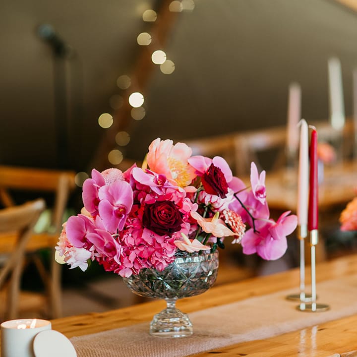 Bowl wedding table flower arrangement with roses, hydrangeas, and orchids with taper candles 