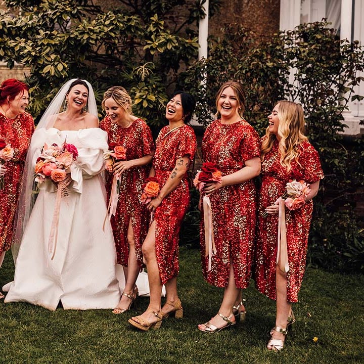 Bridal party wearing red sequin midi bridesmaid dresses with the bride in puff sleeve gown 