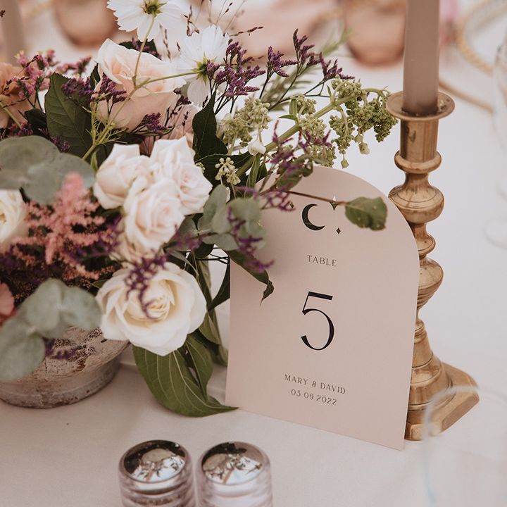 Neutral wedding table number sign next to pink wedding flower arrangements on the table 