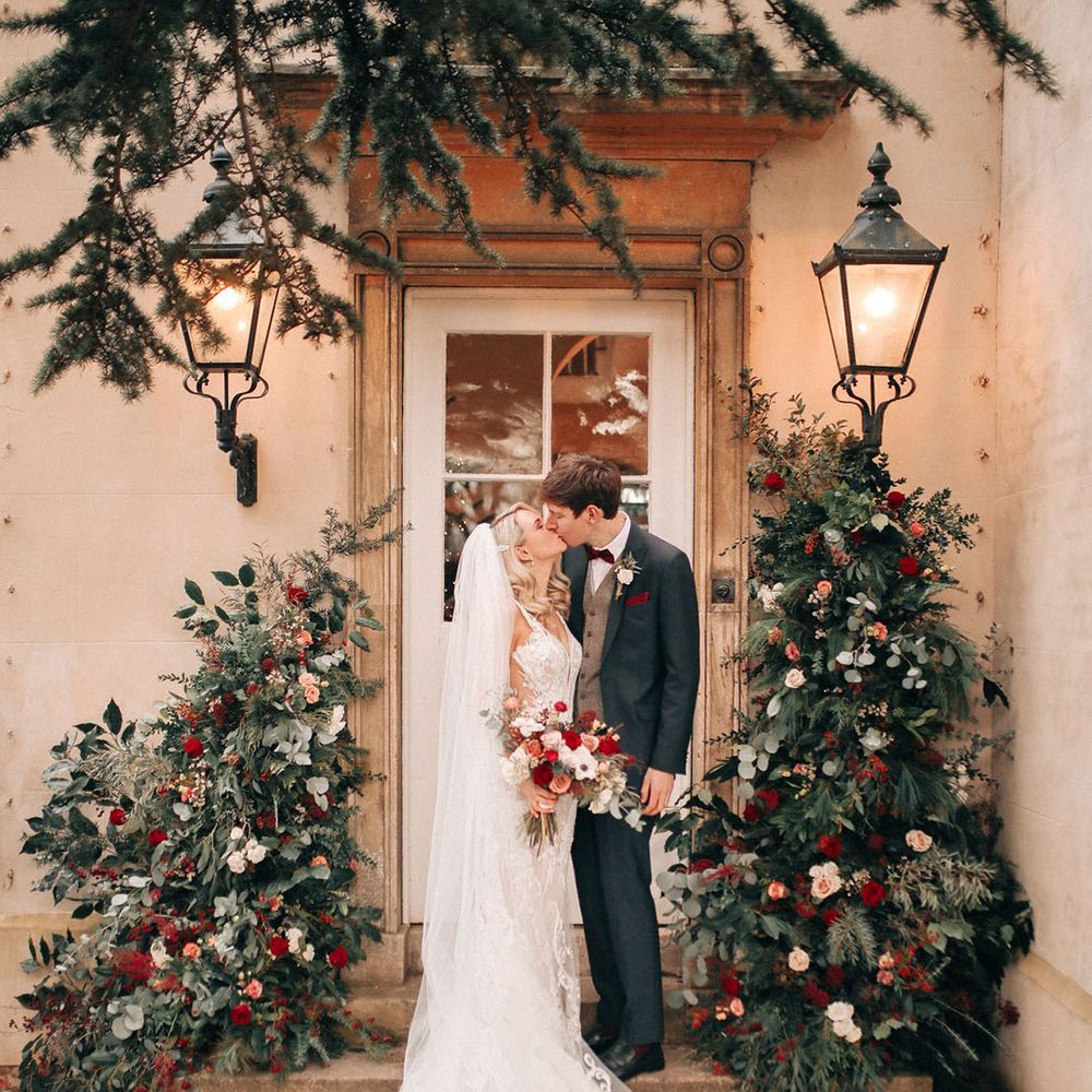 Bride wearing intricate embroidered wedding veil and lace wedding dress in front of red wedding flower decorations 
