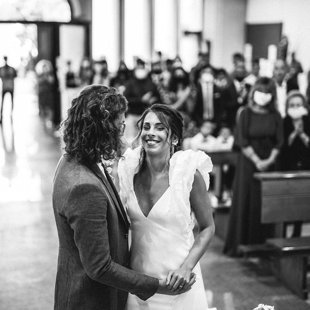 Bride in a ruffle sleeve wedding dress and groom with shoulder length curly hair laughing during their wedding ceremony 