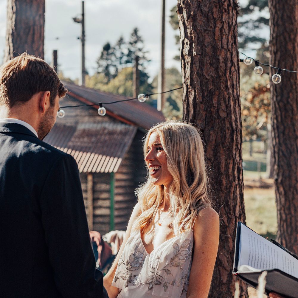 Blonde bride laughs during woodland wedding ceremony