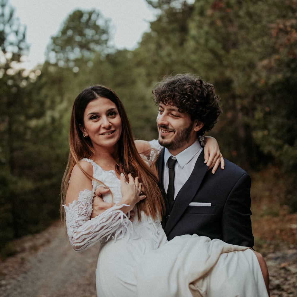 The groom lifting the bride in his arms along a woodland road