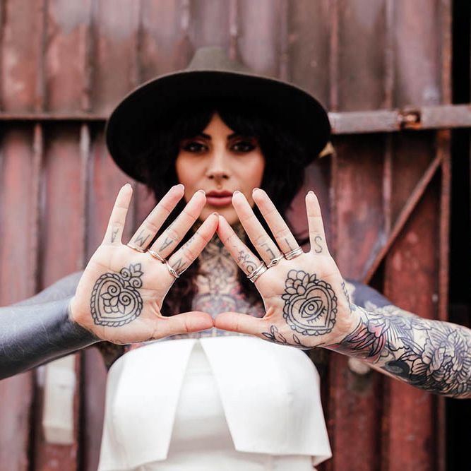 Alternative bride in a strapless wedding dress and fedora hat showing her body art on her hands 