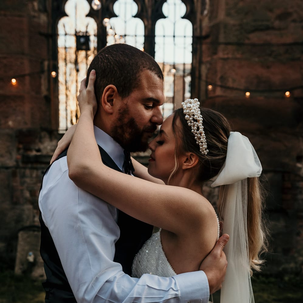 Bride with a pearl headband and bow veil embracing her husband in St Lukes Bombed Out Church in Liverpool 