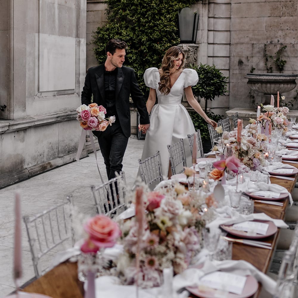 Bride and groom entering their luxury wedding reception with ghost chairs, pink taper candles and floral centrepiece decor 