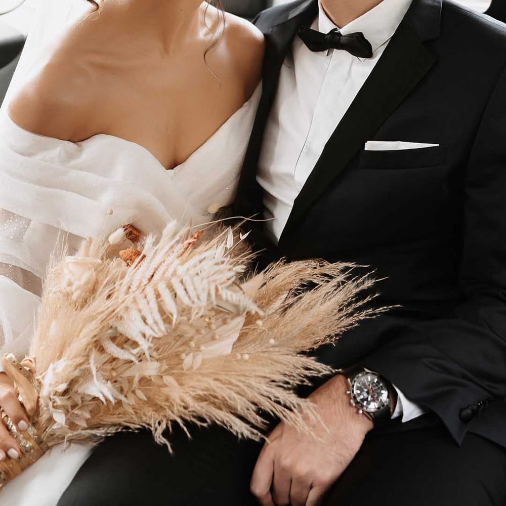 Bride with simple hair up curls wearing drop pearl earrings kissing groom in a black tux with a bow tie 