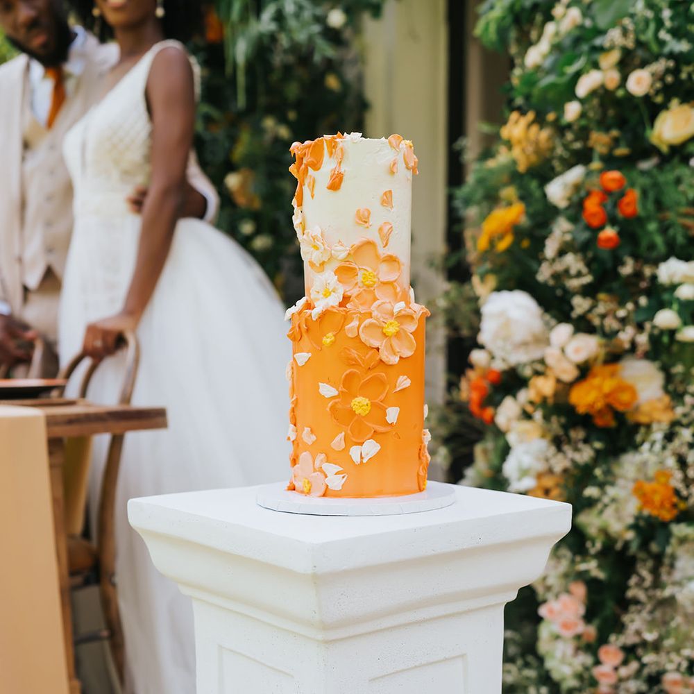 Orange and white buttercream wedding cake with petal decor at outdoor wedding 
