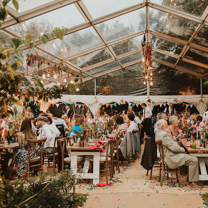 Clear marquee wedding reception with hanging light installations, bunting and foliage decor 