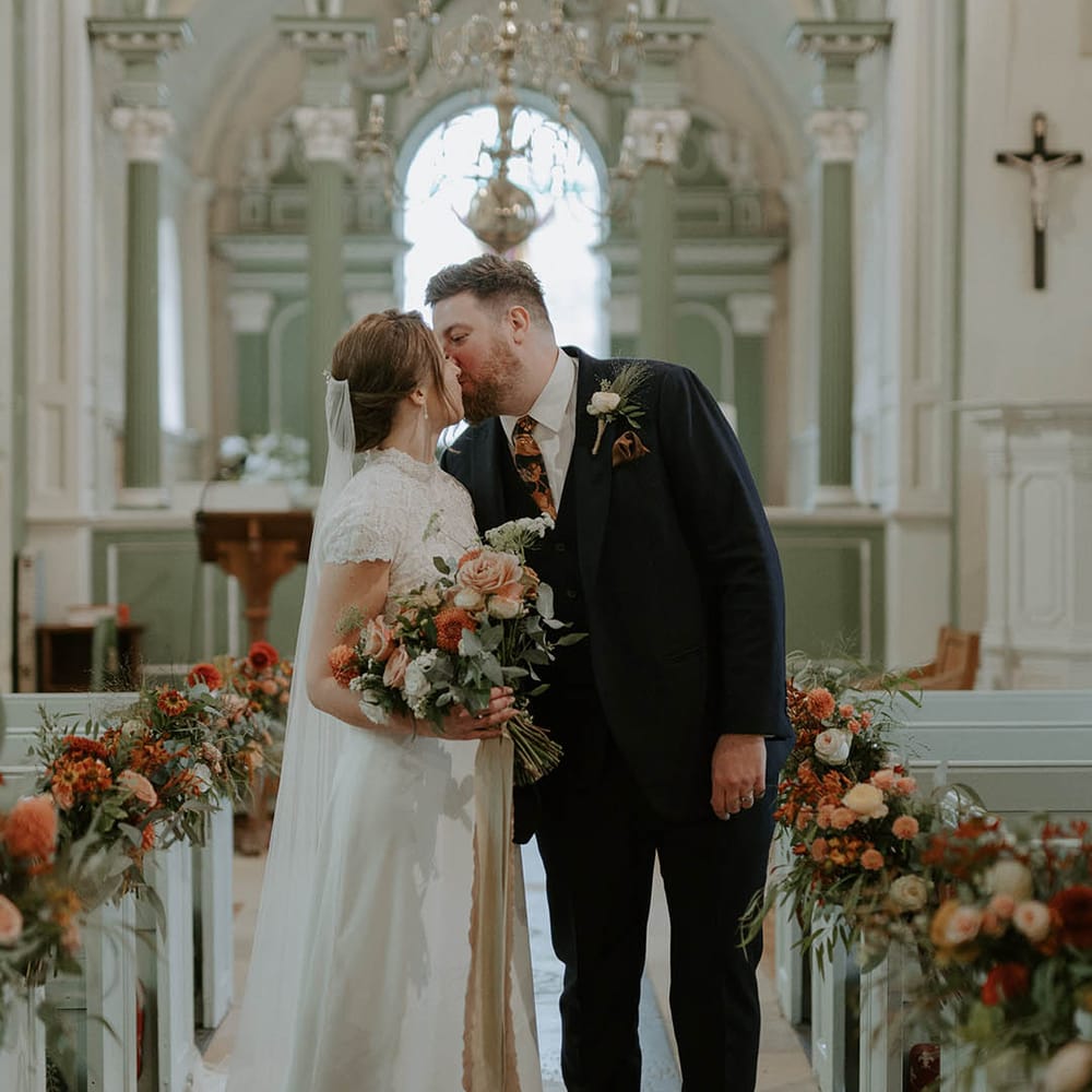 Bride and groom kiss at church ceremony with orange and blush flowers