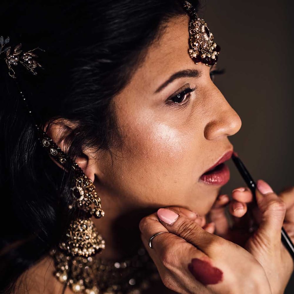 Indian bride gets make up done at her wedding wearing gold jewellery 
