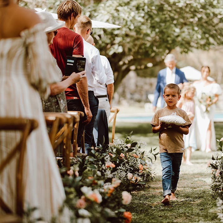 Young ring bearer in jeans walks down the aisle barefoot