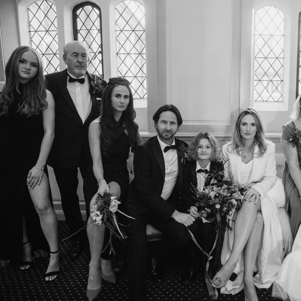 Bride & groom sit with their son and wedding guests at Gosfield Hall on their wedding day in black & white image 
