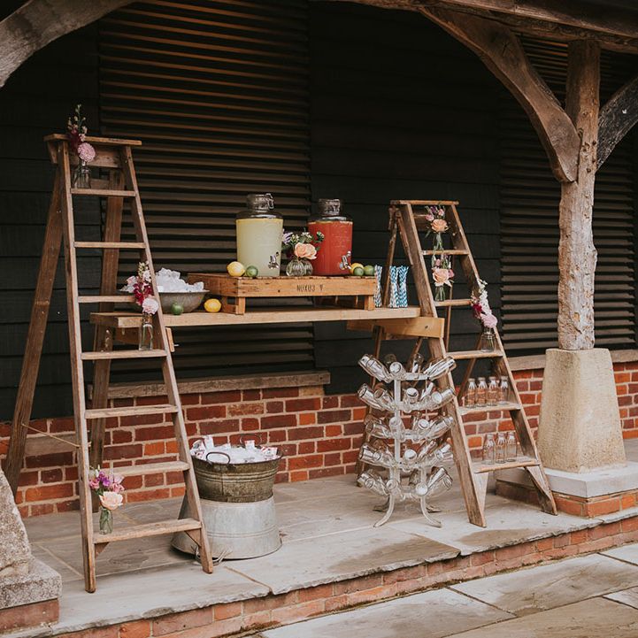 Rustic hydration station made of juices and lemonade with wooden ladders with milk bottles and flowers 