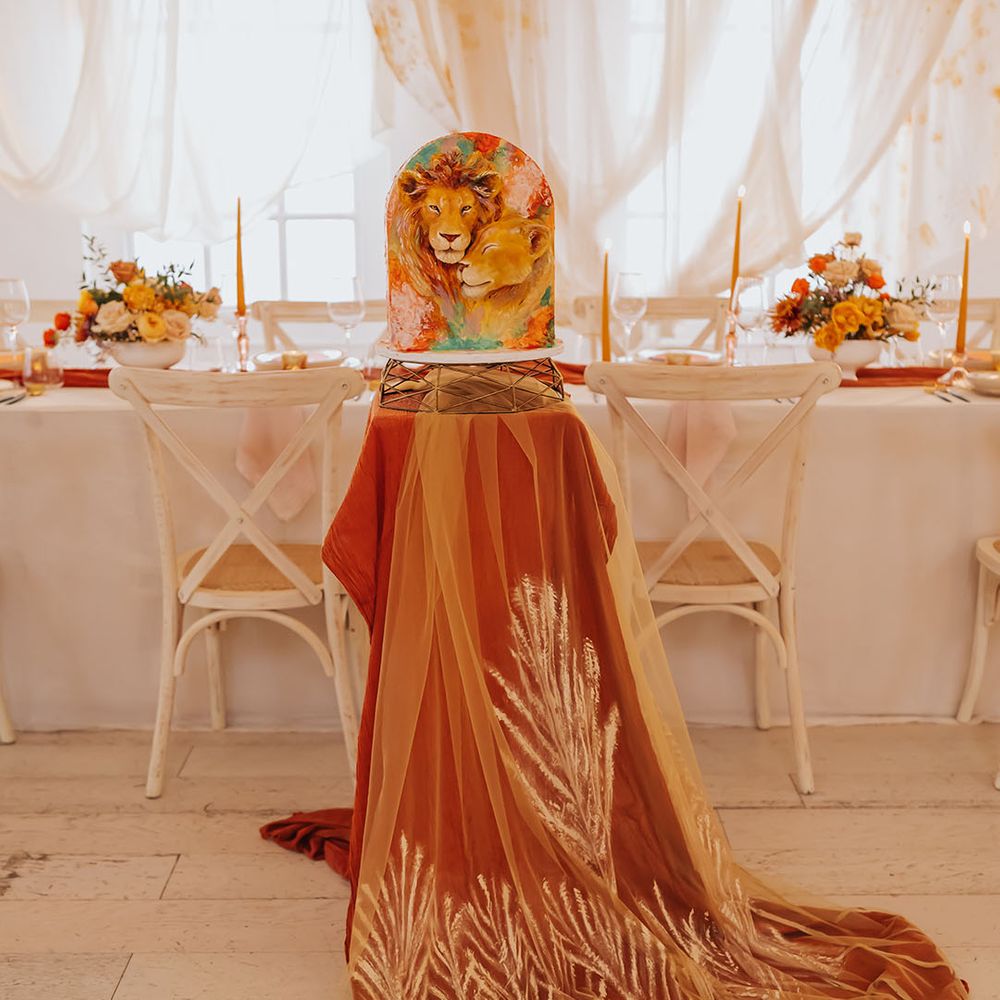 Lion wedding cake on a gold cake stand and burnt orange table cloth and patterned veil