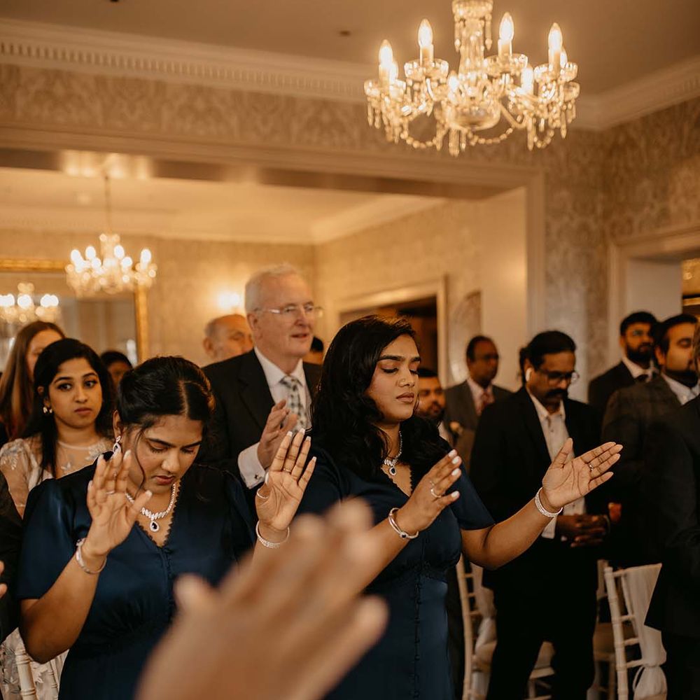 Guests in dark dresses with pearl necklaces and hands raised at Petersham Hotel in Richmond