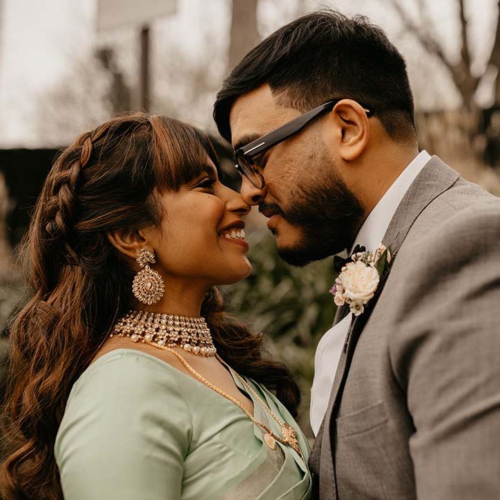 Bride in mint green saree and groom in grey suit smiling, heads touching at multicultural wedding