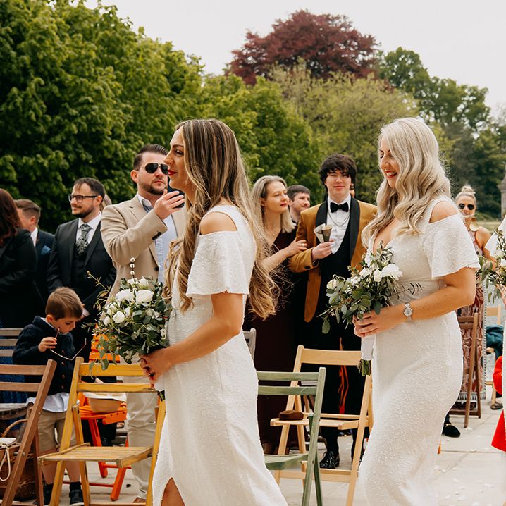 Bridesmaids walk in sparkly white dresses with front slit and white and green classic bouquets 