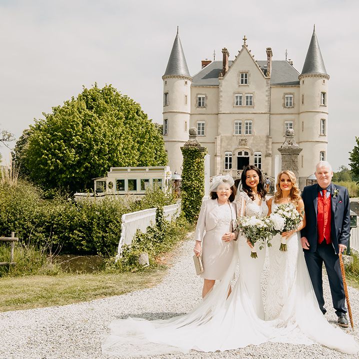 Brides in lace wedding dresses and matching red lipstick with parents outside the chateau 