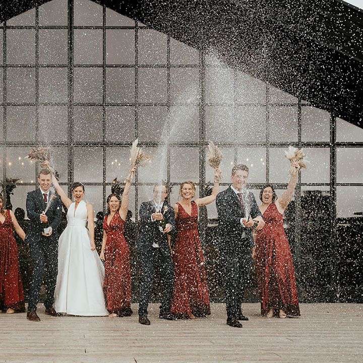 Wedding party in black suits and burgundy bridesmaid dresses at Bottles Hill Barn spraying champagne 