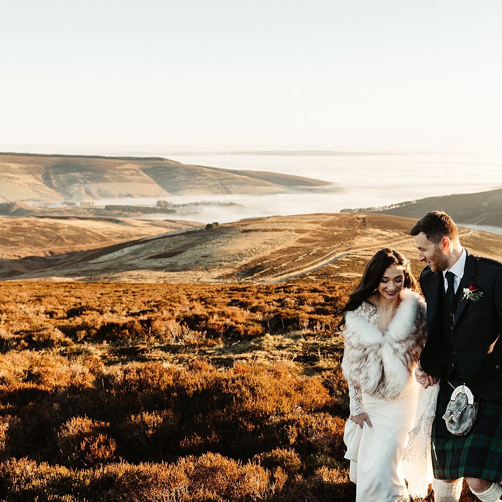 Bride & groom walk across beautiful Scottish hills during sunset on their wedding day