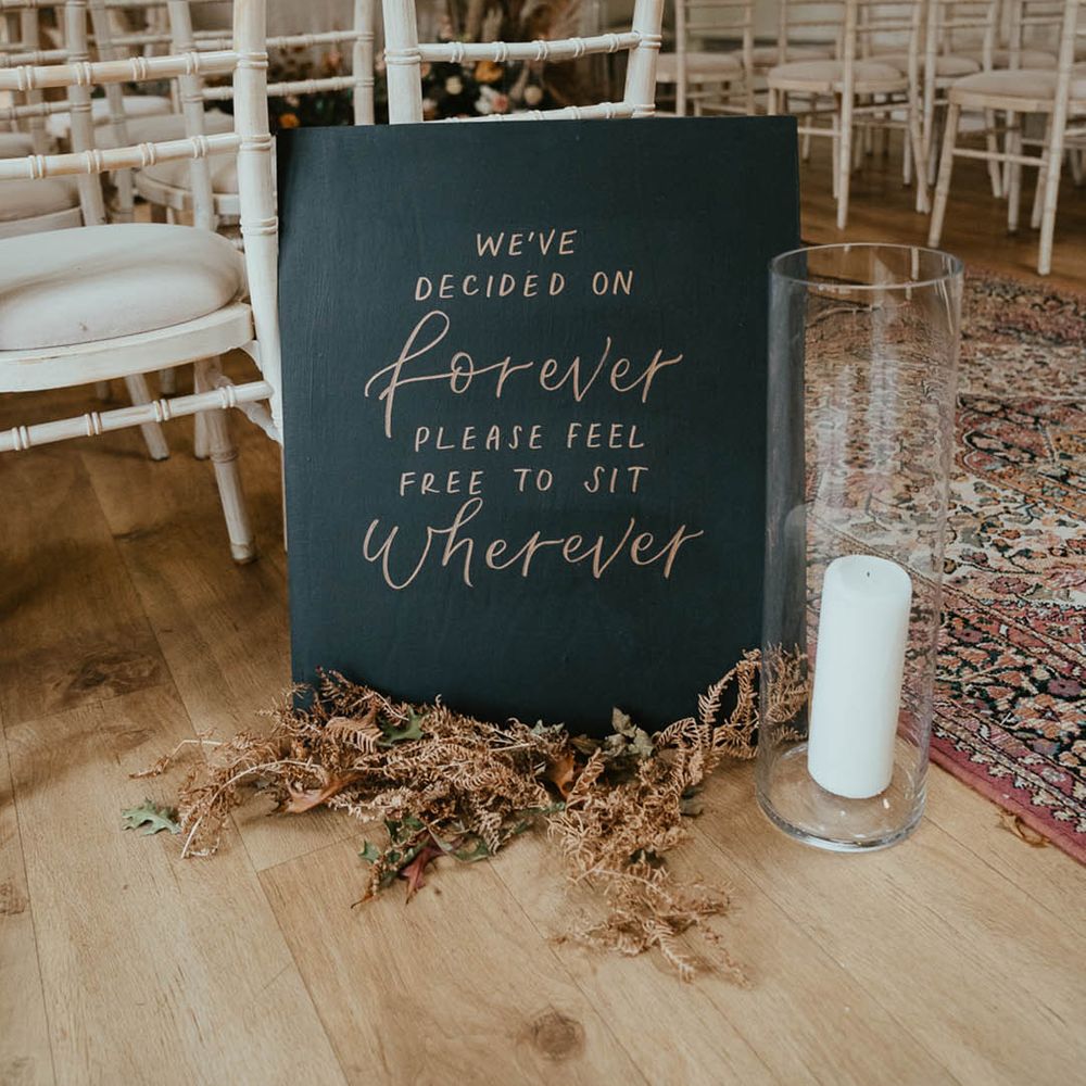 Black and gold sign with dried foliage and a white pillar candle in a hurricane vase 