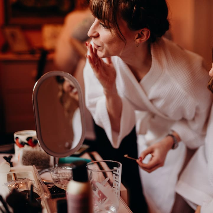 Bride in red lips and getting ready robe and bridesmaid getting ready for Christmas wedding