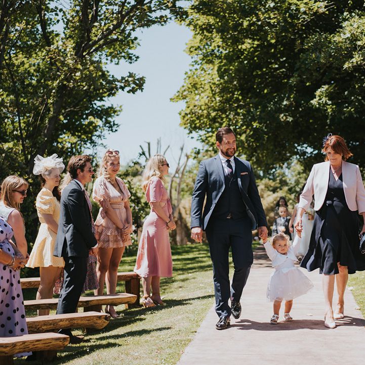 Wedding guests walk down the aisle with flower girl tutu styled dress and sandals 