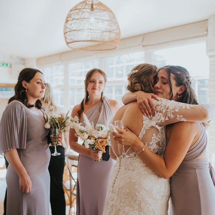 Bride in long sleeve lace wedding dress hugs her bridesmaids on her wedding day 