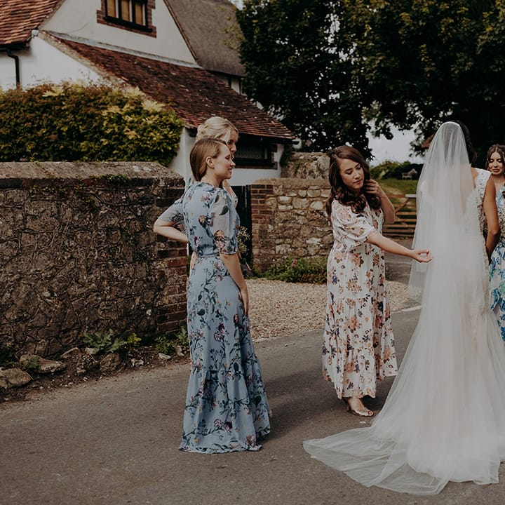 Bridesmaids in mixed floral dresses adjust bride's veil
