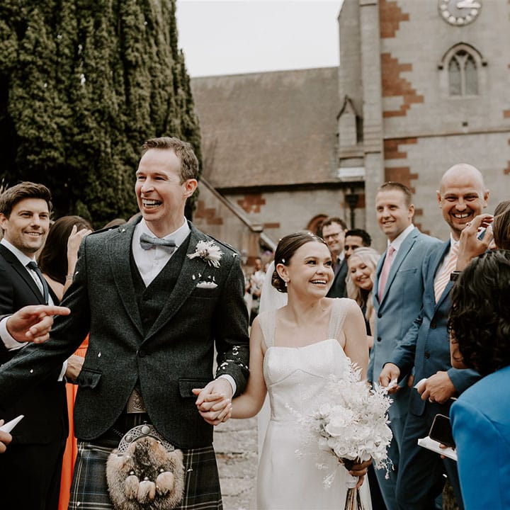 The bride and groom smile as the guests congratulate them and throw confetti over the couple 