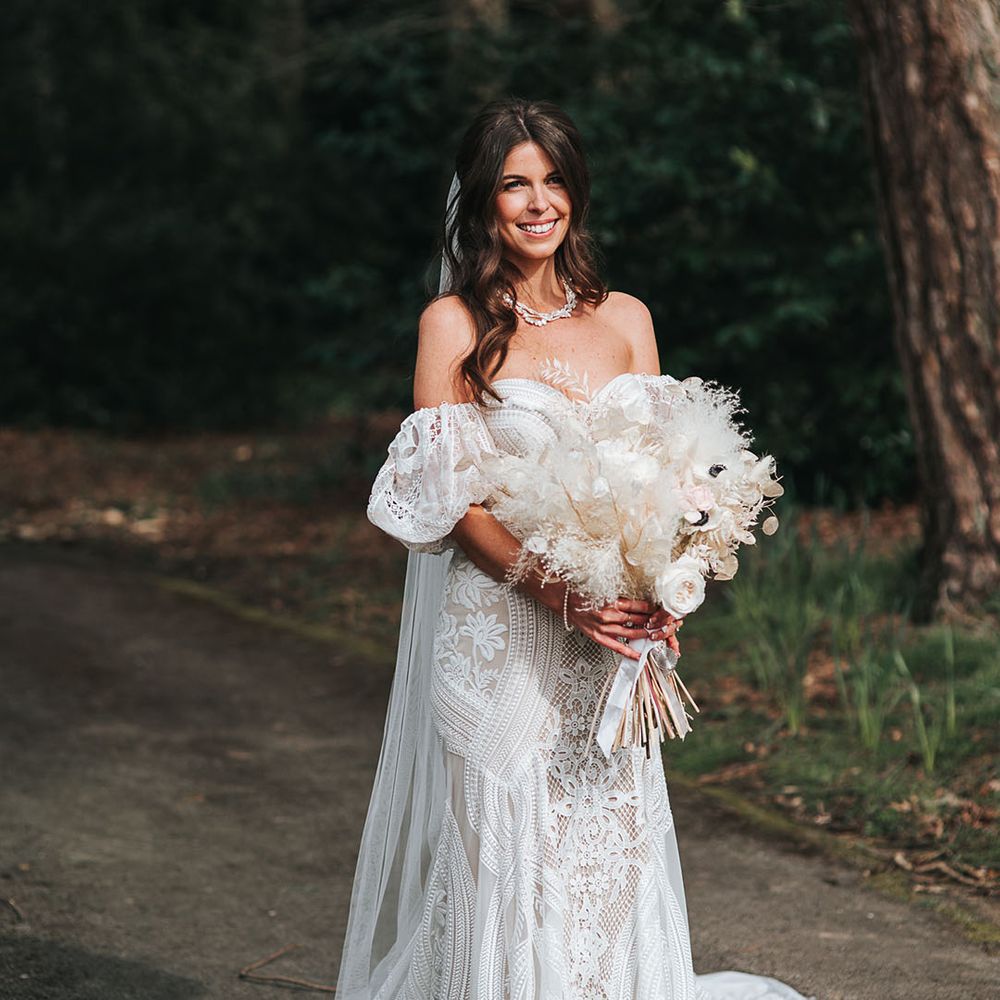 Bride in boho fitted lace wedding dress with train and detachable sleeves with dried white flower bouquet 