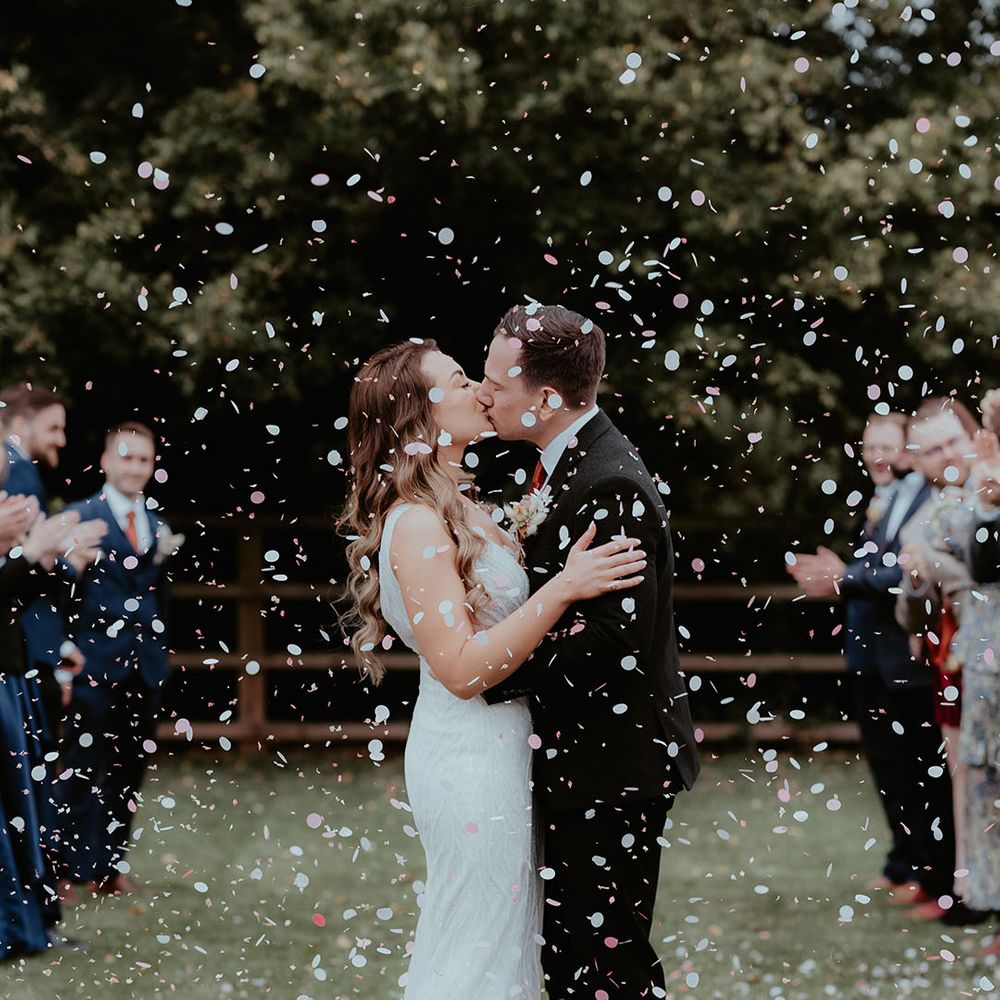 The bride and groom share a kiss to celebrate their wedding day as confetti explodes around them and their guests applaud 