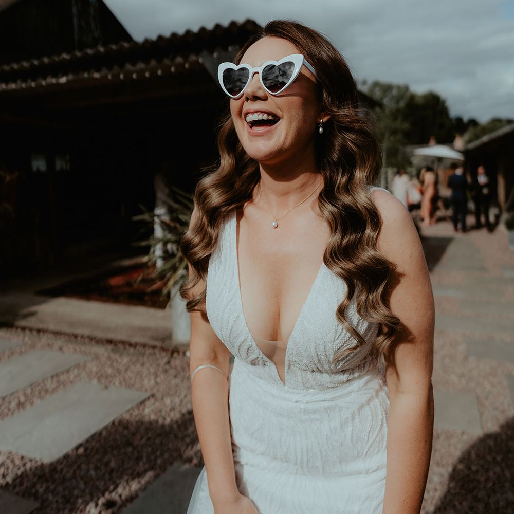Bride laughing with brown hair in waves with a pearl necklace and white retro wedding sunglasses 