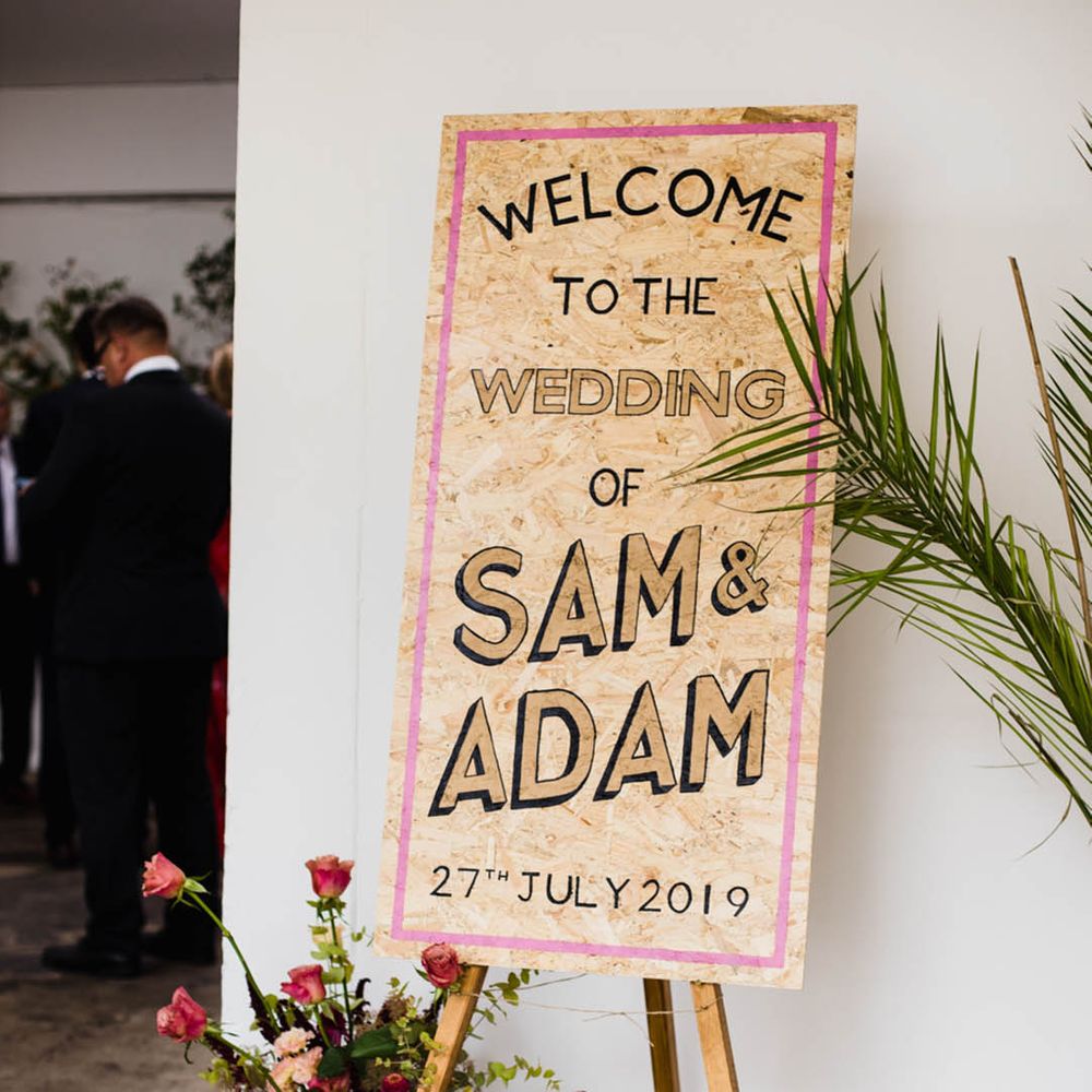 Large chip board welcome wedding sign in black, tan and pink on wooden easel 