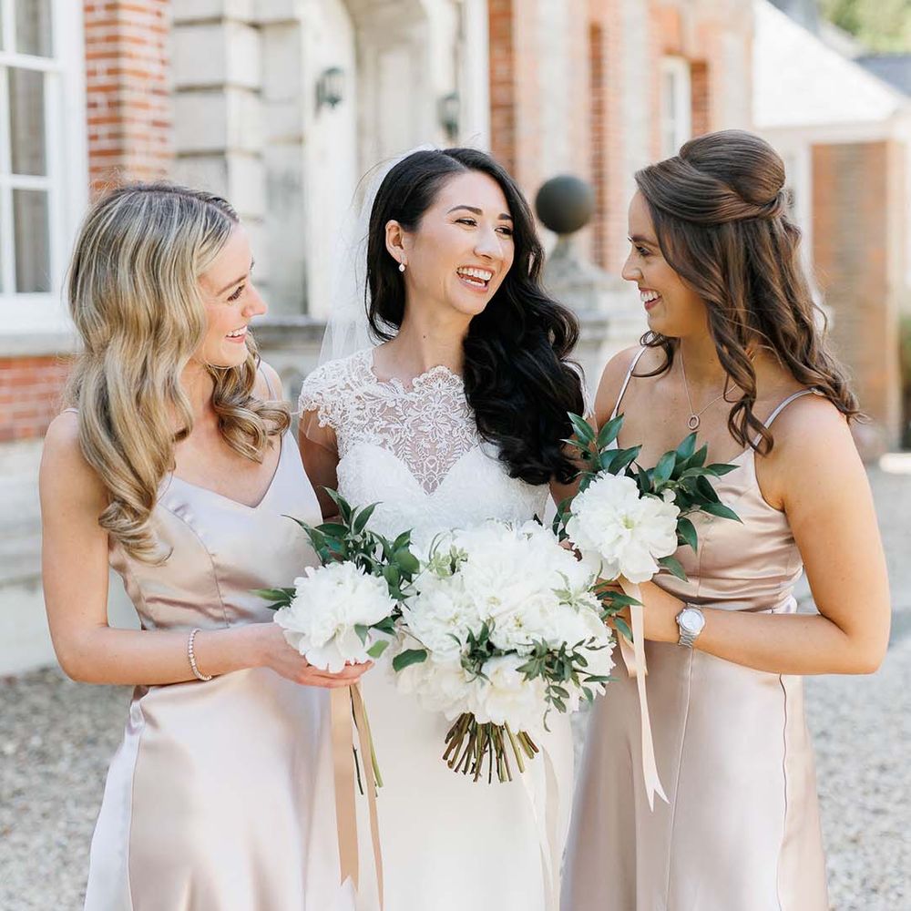 Bride and bridesmaid in pink satin dresses holding white flower bouquets 