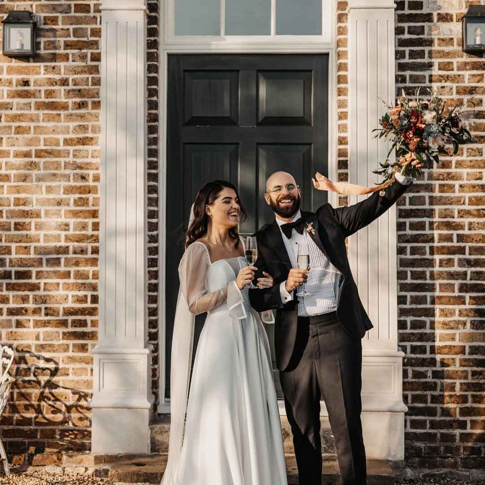Bride in square neck puff sleeve wedding dress and long embroidered wedding veil standing with groom in classic black tuxedo with black bowtie 