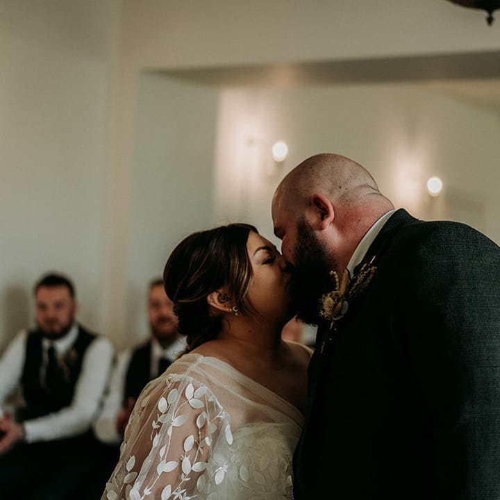 Groom in green tweed wedding suit kissing bride for the first time as a married couple