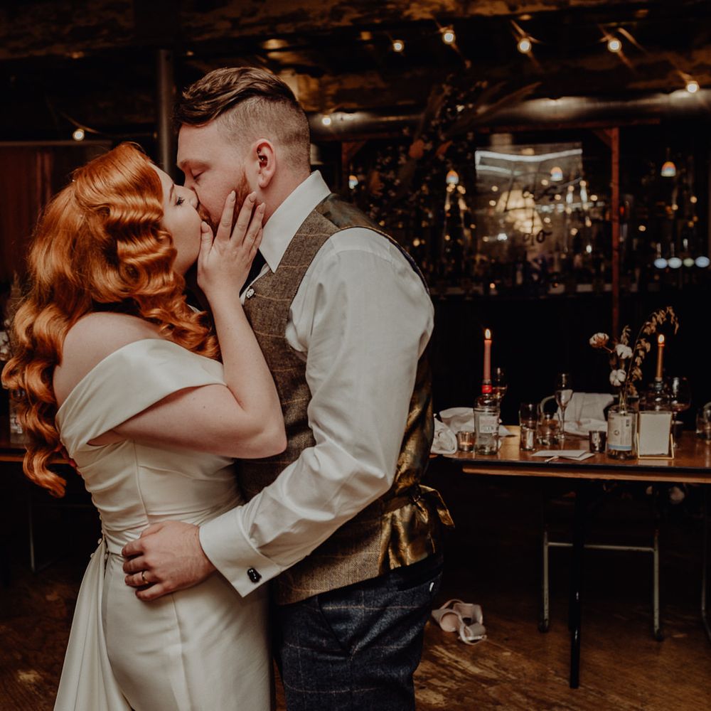 Bride with vintage wedding hair kissing her groom at evening reception 