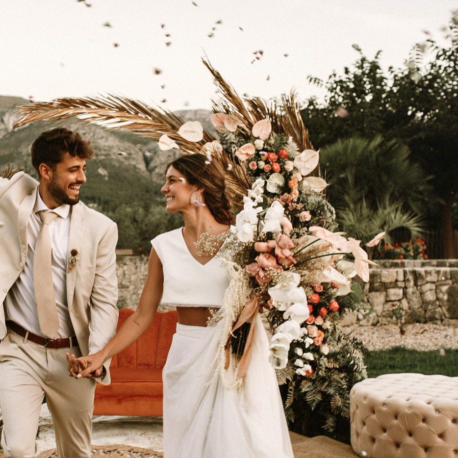 Confetti moment with boho bride in separates, groom in a beige suit with a boho wedding flowers arch 