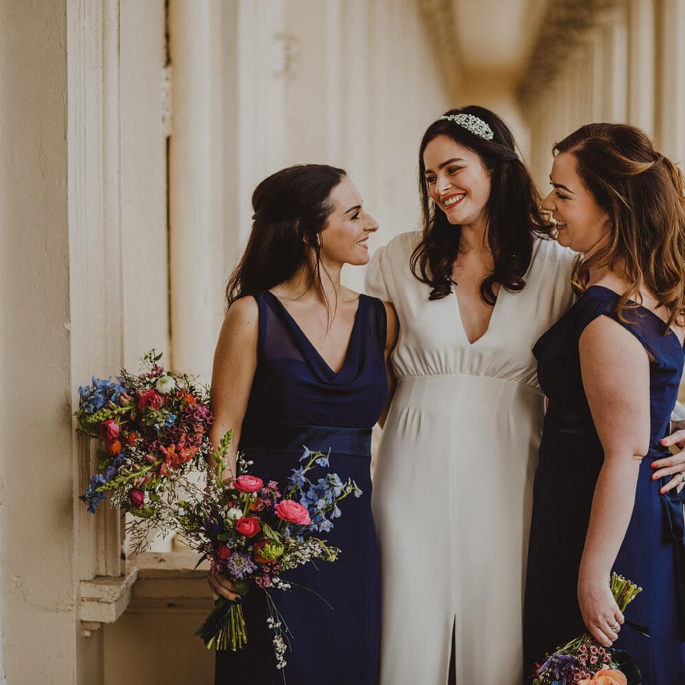 Bride with her two bridesmaids wearing navy maids to measure dresses 