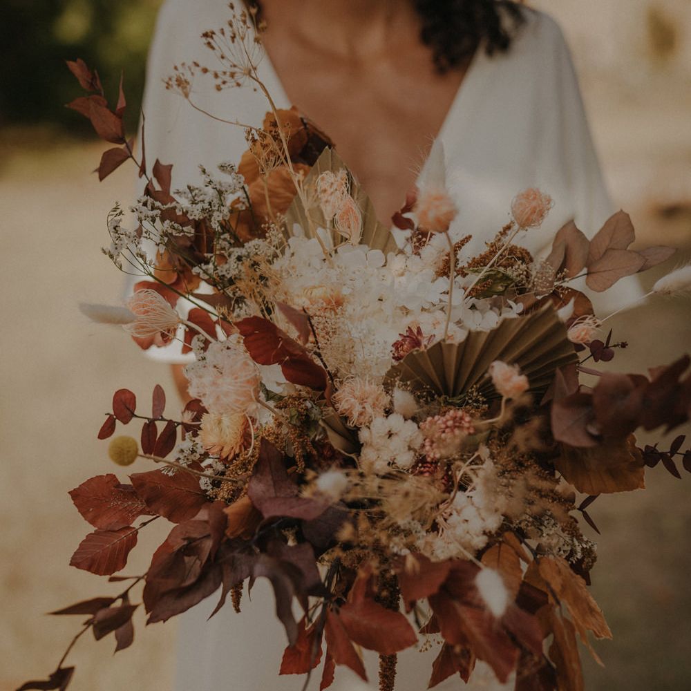 Bride holding an autumn wedding bouquet with brown leaves, dried palms, and white flowers 