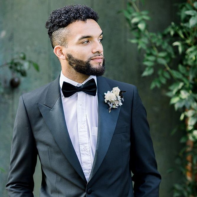 Bearded groom in a tuxedo and bow tie with white buttonhole flower 