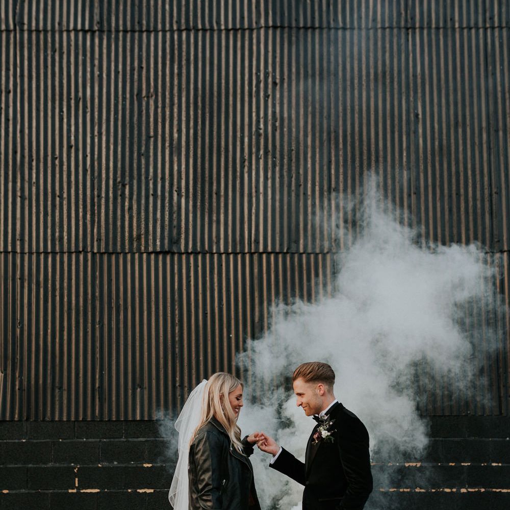 White smoke bomb wedding portrait with the bride in a personalised leather jacket and the groom in a tuxedo 