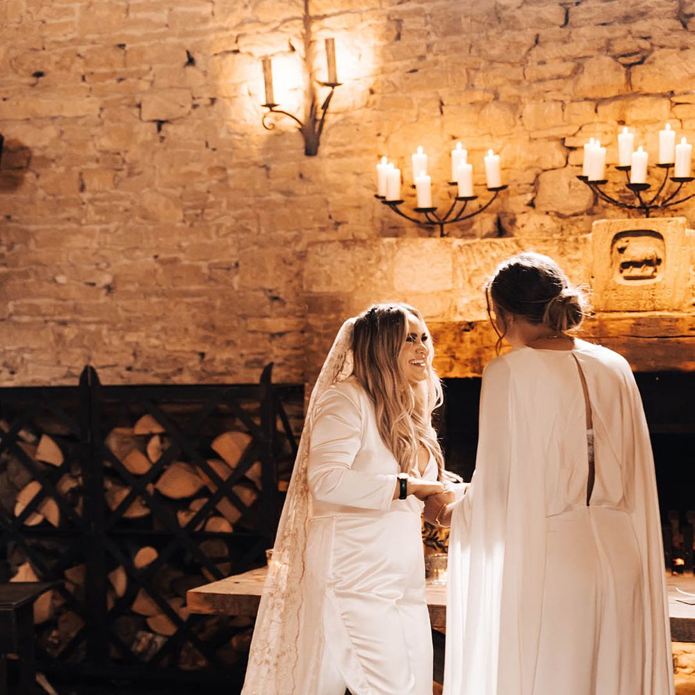 Brides look lovingly at one another as they hold hands and smile during ceremony