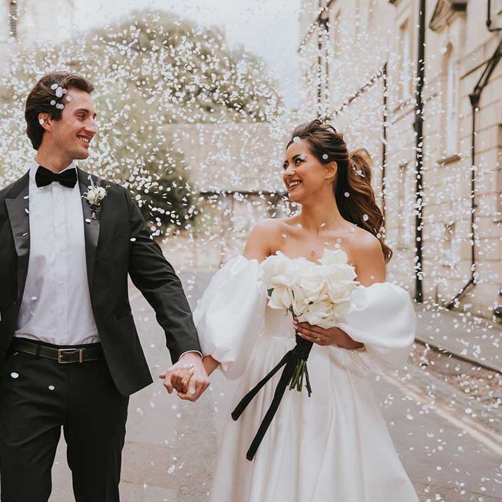 White confetti moment at black tie wedding with groom in a tuxedo and bride in a strapless wedding dress holding a white rose wedding bouquet 