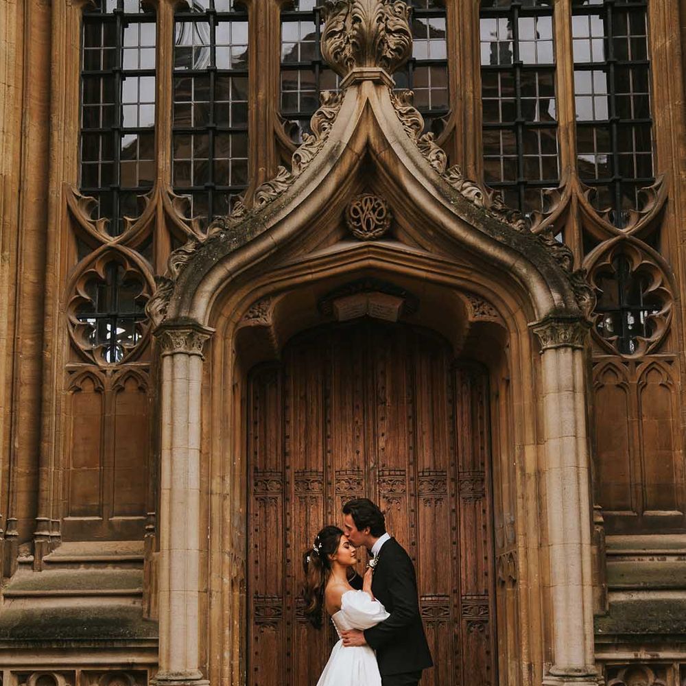Groom in a tuxedo kissing his brides forehead at the historic doors of Bodleian Library 