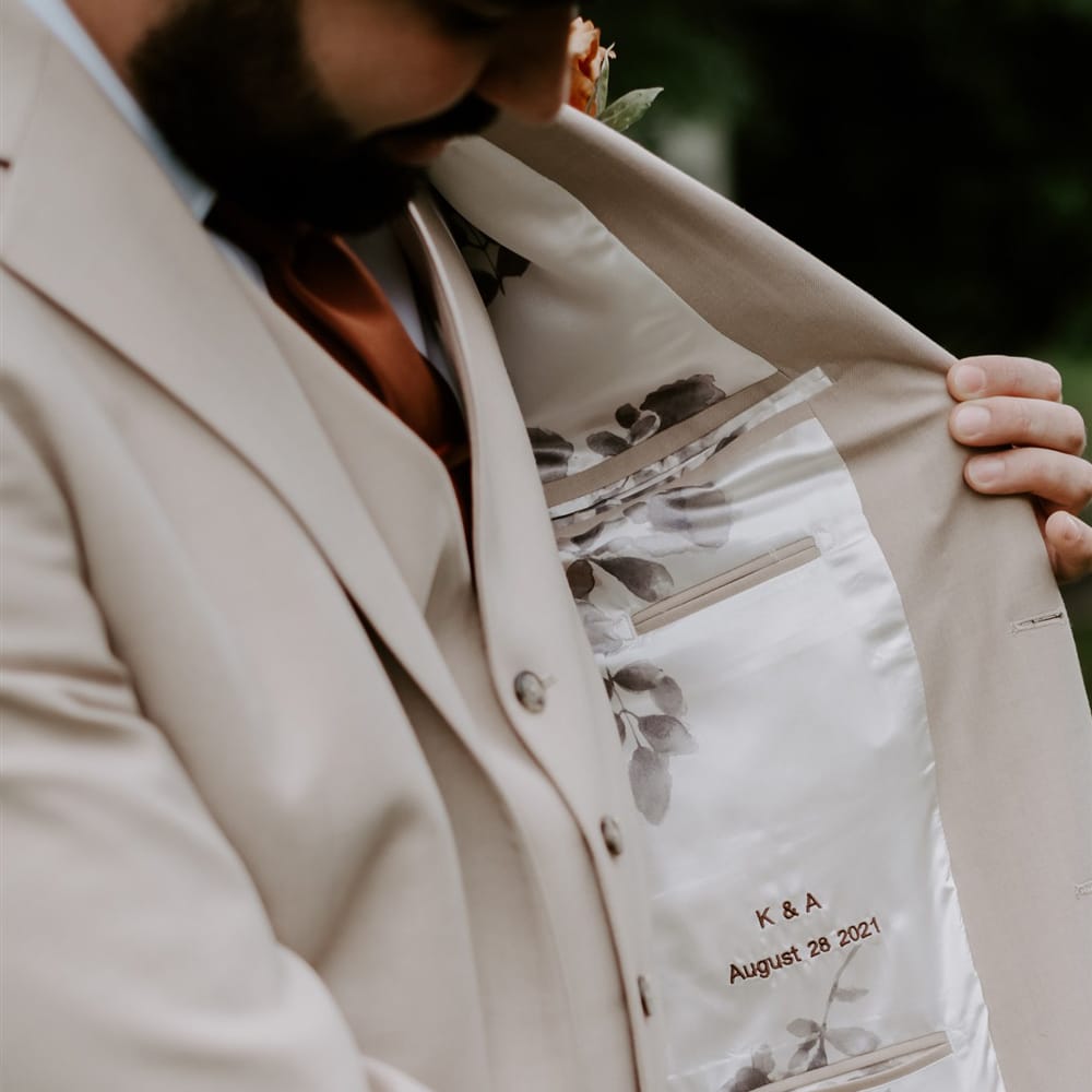 Stitching in lining of grooms beige suit jacket reading 'K & A August 28 2021' for DIY garden wedding in Bedfordshire