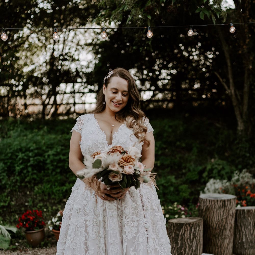 Plus size bride in homemade lace wedding dress with train holding mixed rose bridal bouquet stands in garden after wedding ceremony